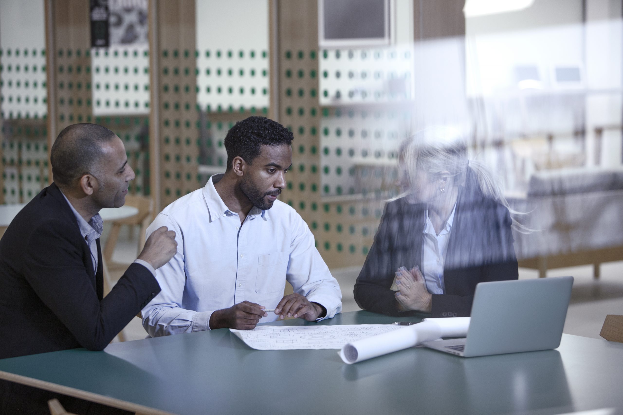 Co-workers collaborating over blueprints in front of a laptop